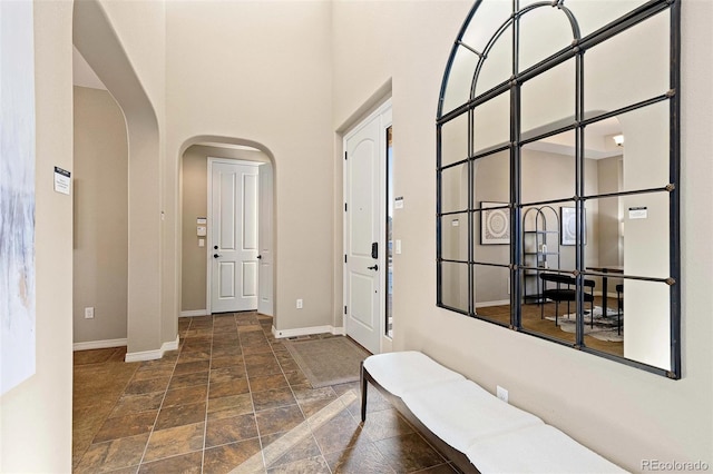 foyer featuring arched walkways, stone finish flooring, a high ceiling, and baseboards