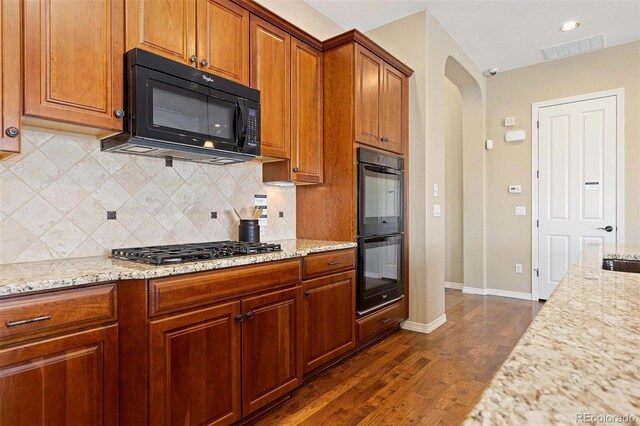 kitchen featuring visible vents, arched walkways, dark wood-type flooring, light stone countertops, and black appliances