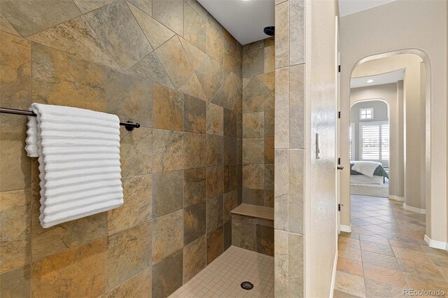 ensuite bathroom featuring ensuite bathroom, a tile shower, and baseboards