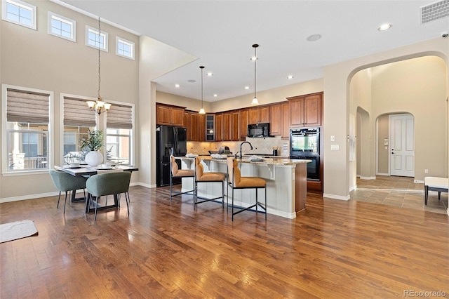 kitchen with black appliances, arched walkways, brown cabinets, a kitchen island with sink, and a breakfast bar area