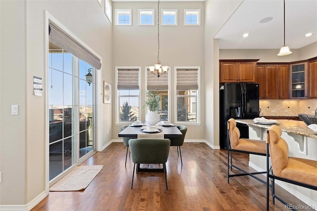 dining area featuring a chandelier, dark wood-type flooring, baseboards, and a towering ceiling