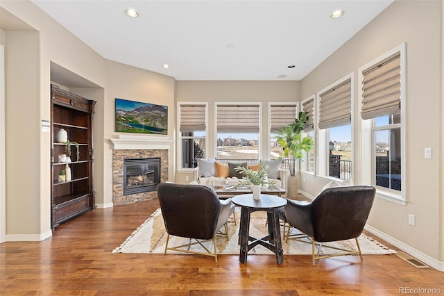 living area featuring wood finished floors, a stone fireplace, recessed lighting, and baseboards
