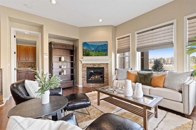 living area with wood finished floors, a stone fireplace, and recessed lighting