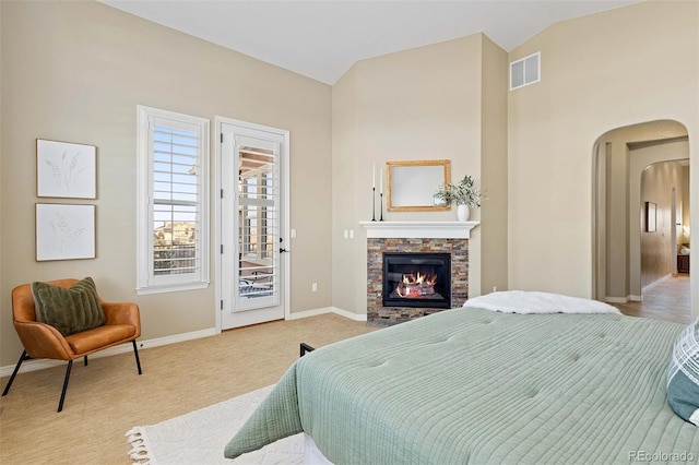 bedroom featuring access to exterior, arched walkways, a stone fireplace, baseboards, and vaulted ceiling