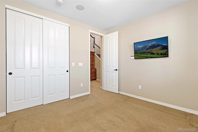 unfurnished bedroom featuring light carpet, baseboards, and a closet