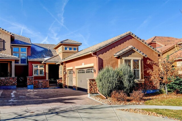 view of front of property featuring a garage, driveway, stucco siding, a tile roof, and stone siding
