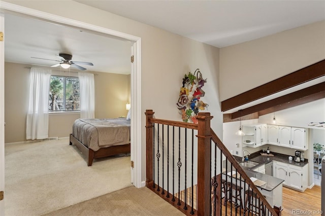 bedroom with ceiling fan, baseboards, light colored carpet, beam ceiling, and a sink