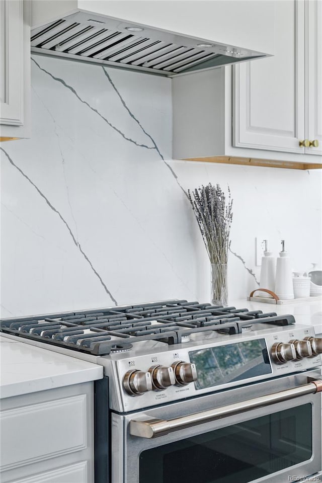 4978 Camel Heights Rd, Evergreen, CO 80439 - kitchen view of stainless steel gas stove, custom exhaust hood, white cabinets, decorative backsplash, and light stone countertops