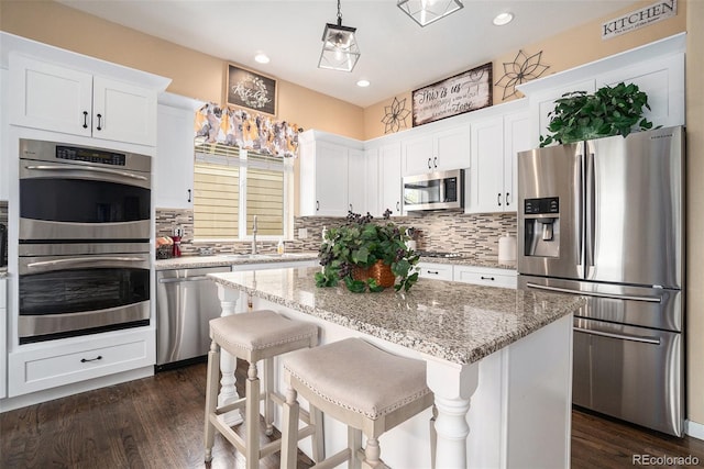 2726 Aylesbury Way, Johnstown, CO 80534 - kitchen featuring appliances with stainless steel finishes, white cabinetry, tasteful backsplash, a center island, and dark wood-style floors