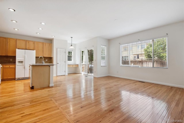 kitchen featuring hanging light fixtures, light hardwood / wood-style flooring, an island with sink, decorative backsplash, and white fridge with ice dispenser