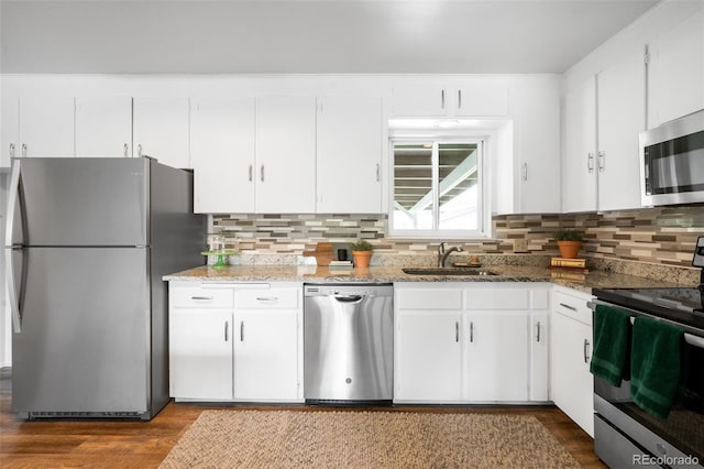 kitchen with appliances with stainless steel finishes, a sink, decorative backsplash, stone counters, and white cabinets