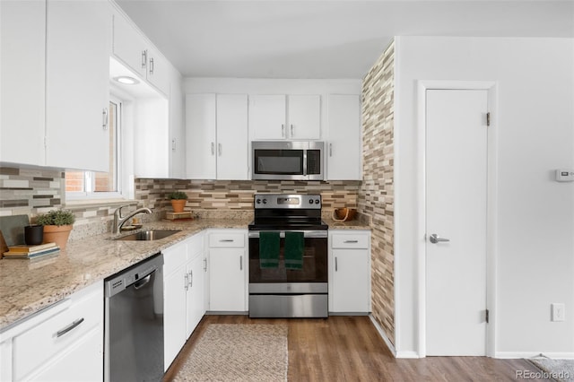 kitchen featuring appliances with stainless steel finishes, a sink, wood finished floors, and white cabinetry