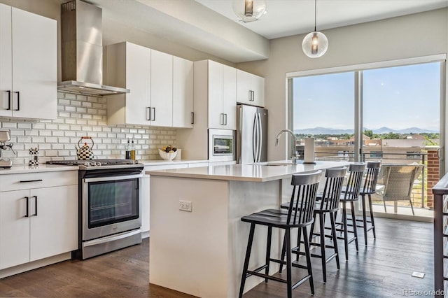 kitchen featuring stainless steel appliances, white cabinetry, a kitchen island with sink, and wall chimney range hood