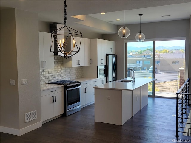 kitchen featuring white cabinetry, decorative light fixtures, a center island with sink, stainless steel appliances, and backsplash