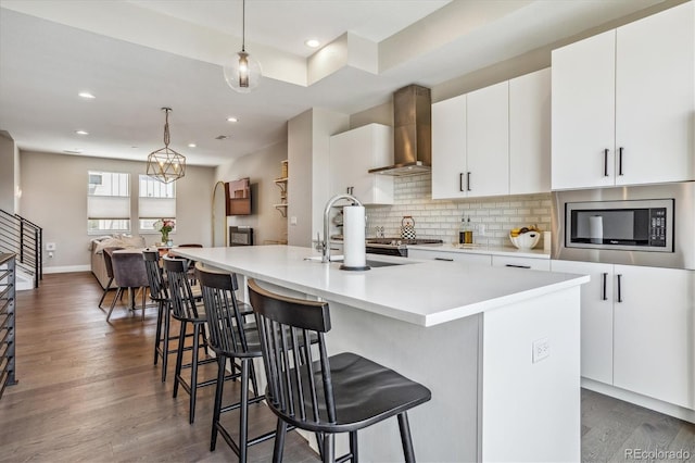 kitchen with stainless steel microwave, decorative light fixtures, a kitchen island with sink, and range hood