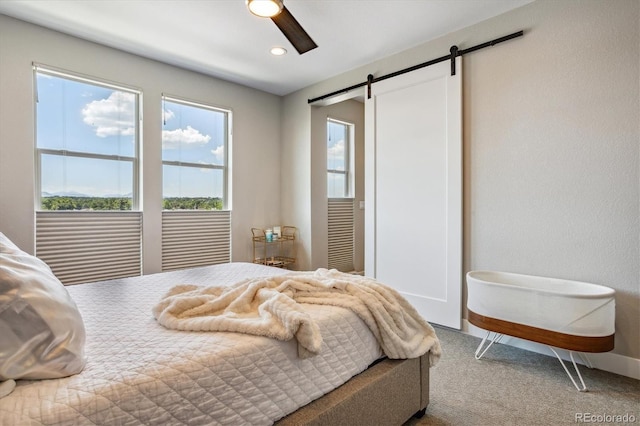 carpeted bedroom with a barn door and ceiling fan