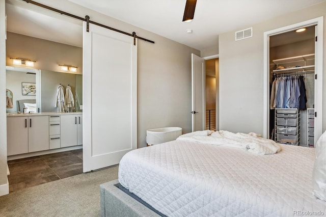 bedroom featuring ceiling fan, a barn door, dark carpet, a walk in closet, and a closet