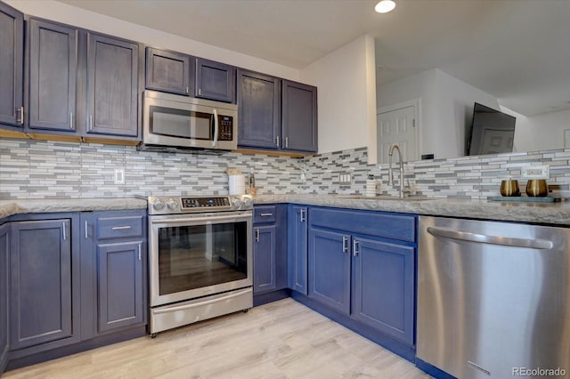 kitchen with light stone countertops, light wood-style flooring, a sink, stainless steel appliances, and backsplash