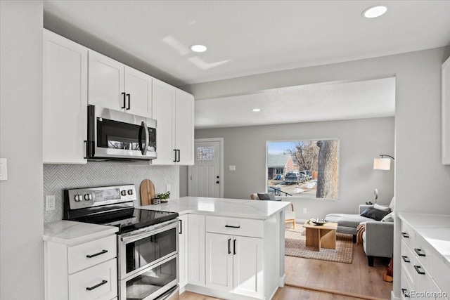 kitchen with appliances with stainless steel finishes, open floor plan, a peninsula, white cabinetry, and backsplash