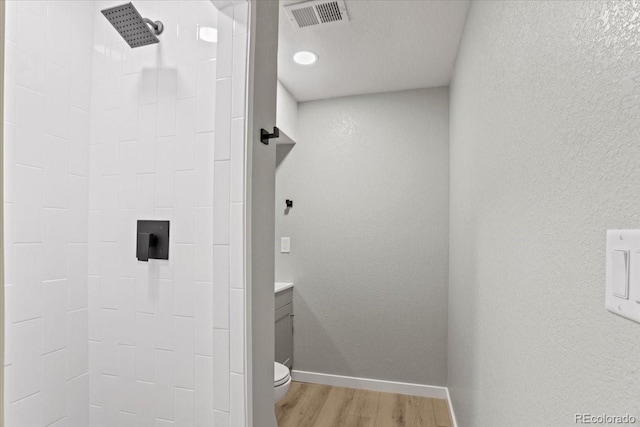 full bathroom with visible vents, toilet, a tile shower, wood finished floors, and baseboards