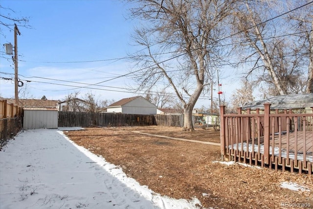 snowy yard featuring a fenced backyard, an outbuilding, a deck, and a shed