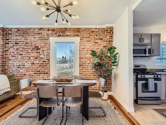 dining area with a notable chandelier, brick wall, light wood-type flooring, and a wealth of natural light