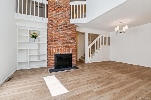 2881 W Long Dr Unit F, Littleton, CO 80120 - unfurnished living room with a towering ceiling, stairs, wood finished floors, a chandelier, and a brick fireplace