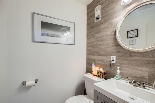 half bathroom featuring vanity, wooden walls, and toilet