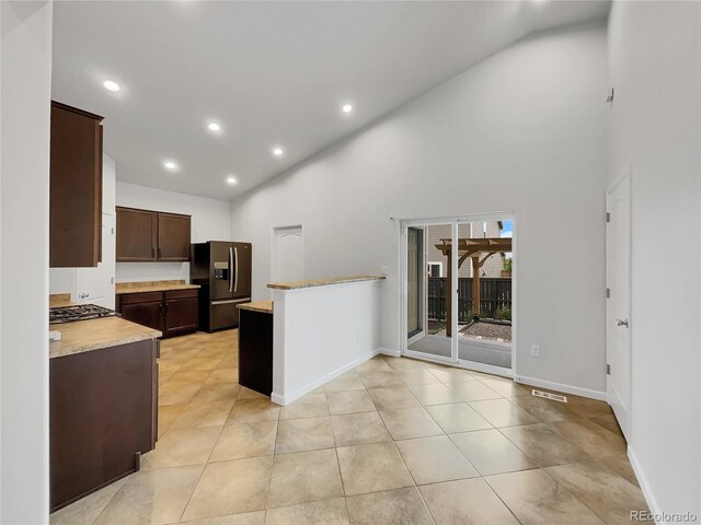 kitchen with high vaulted ceiling, stainless steel gas cooktop, light tile patterned floors, dark brown cabinetry, and black fridge