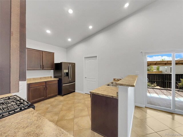 kitchen featuring light tile patterned flooring, dark brown cabinetry, sink, high vaulted ceiling, and stainless steel fridge