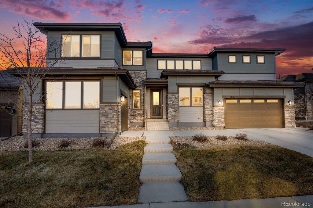 prairie-style home featuring an attached garage, stone siding, and driveway