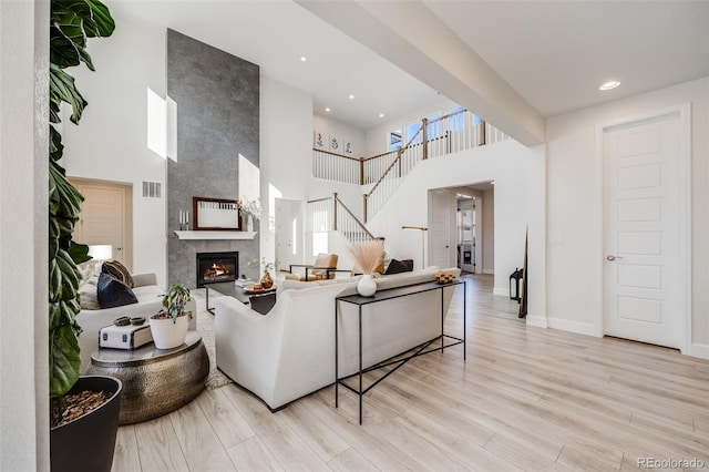 living room featuring light wood-style flooring, a large fireplace, visible vents, a towering ceiling, and baseboards