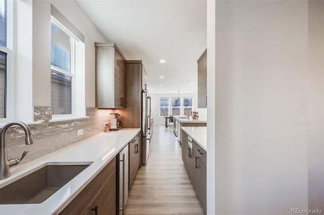 kitchen with high end refrigerator, a sink, light countertops, backsplash, and recessed lighting