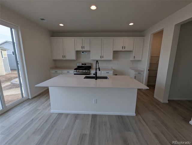 kitchen with white cabinetry, stainless steel gas stove, sink, light hardwood / wood-style flooring, and an island with sink