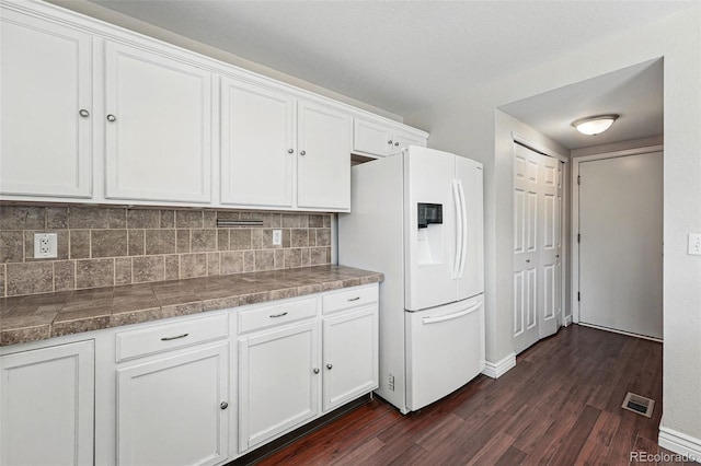 kitchen with tasteful backsplash, visible vents, dark wood-style flooring, white cabinetry, and white refrigerator with ice dispenser