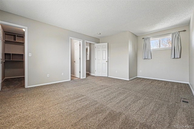 unfurnished bedroom featuring carpet flooring, a textured ceiling, visible vents, and a walk in closet