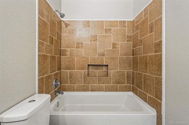 bathroom featuring toilet, washtub / shower combination, and a textured wall