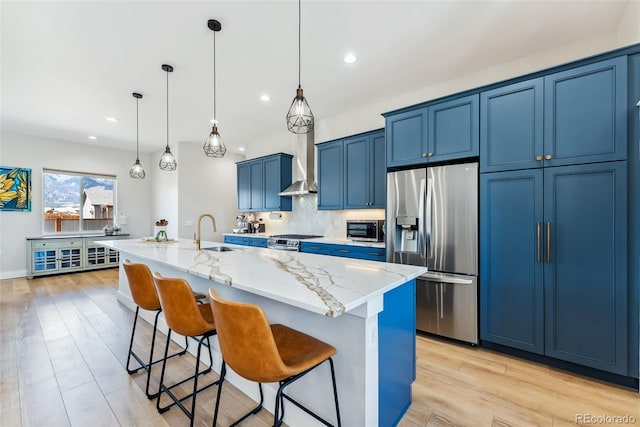 kitchen with a sink, a center island with sink, a kitchen bar, blue cabinets, and appliances with stainless steel finishes