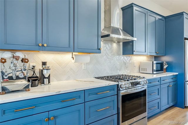 kitchen with blue cabinets, wall chimney range hood, and stainless steel appliances