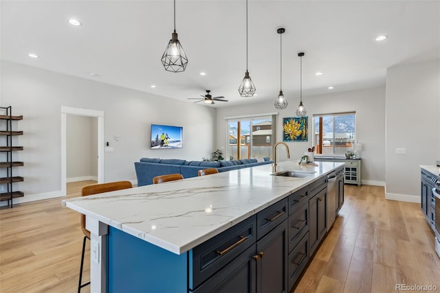 kitchen featuring a ceiling fan, an island with sink, a kitchen bar, light wood-type flooring, and a sink