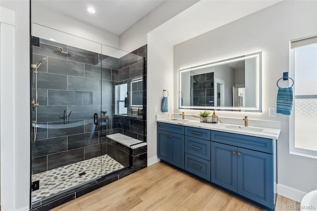 bathroom featuring double vanity, a shower stall, a sink, and wood finished floors