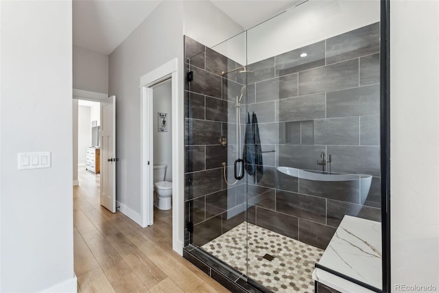 bathroom with toilet, baseboards, a shower stall, and wood finished floors