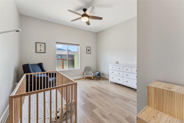 bedroom with a nursery area, ceiling fan, baseboards, and light wood-style flooring