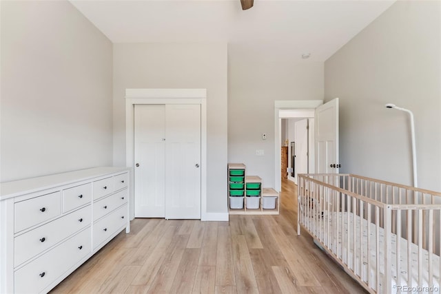 bedroom with a nursery area, baseboards, a closet, and light wood finished floors