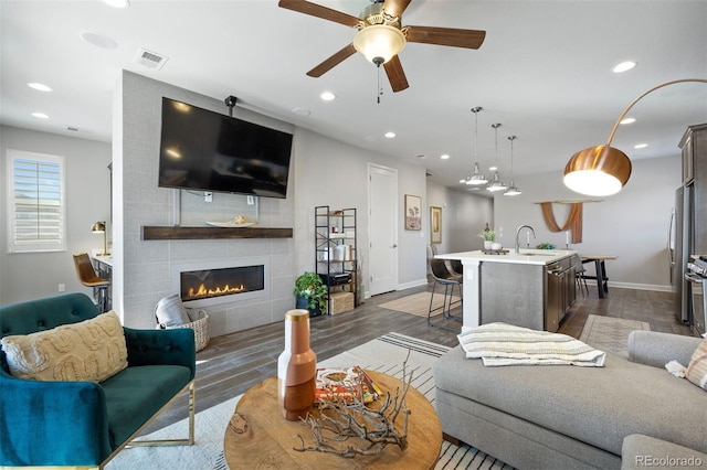 living room with ceiling fan, dark hardwood / wood-style floors, a tiled fireplace, and sink