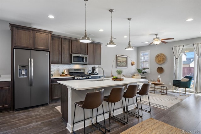 kitchen featuring sink, hanging light fixtures, dark brown cabinets, stainless steel appliances, and an island with sink