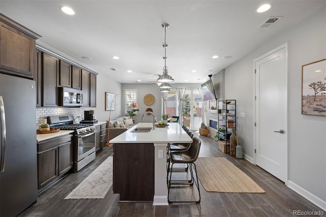 kitchen featuring a kitchen island with sink, sink, dark brown cabinetry, and appliances with stainless steel finishes