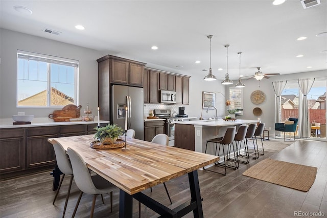 kitchen featuring pendant lighting, sink, stainless steel appliances, dark brown cabinets, and a center island with sink