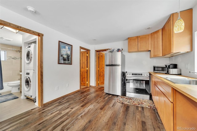 kitchen featuring sink, dark wood-type flooring, hanging light fixtures, stainless steel appliances, and stacked washer / drying machine