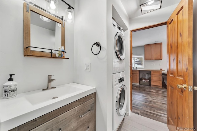 clothes washing area with stacked washer and dryer, sink, and light hardwood / wood-style flooring